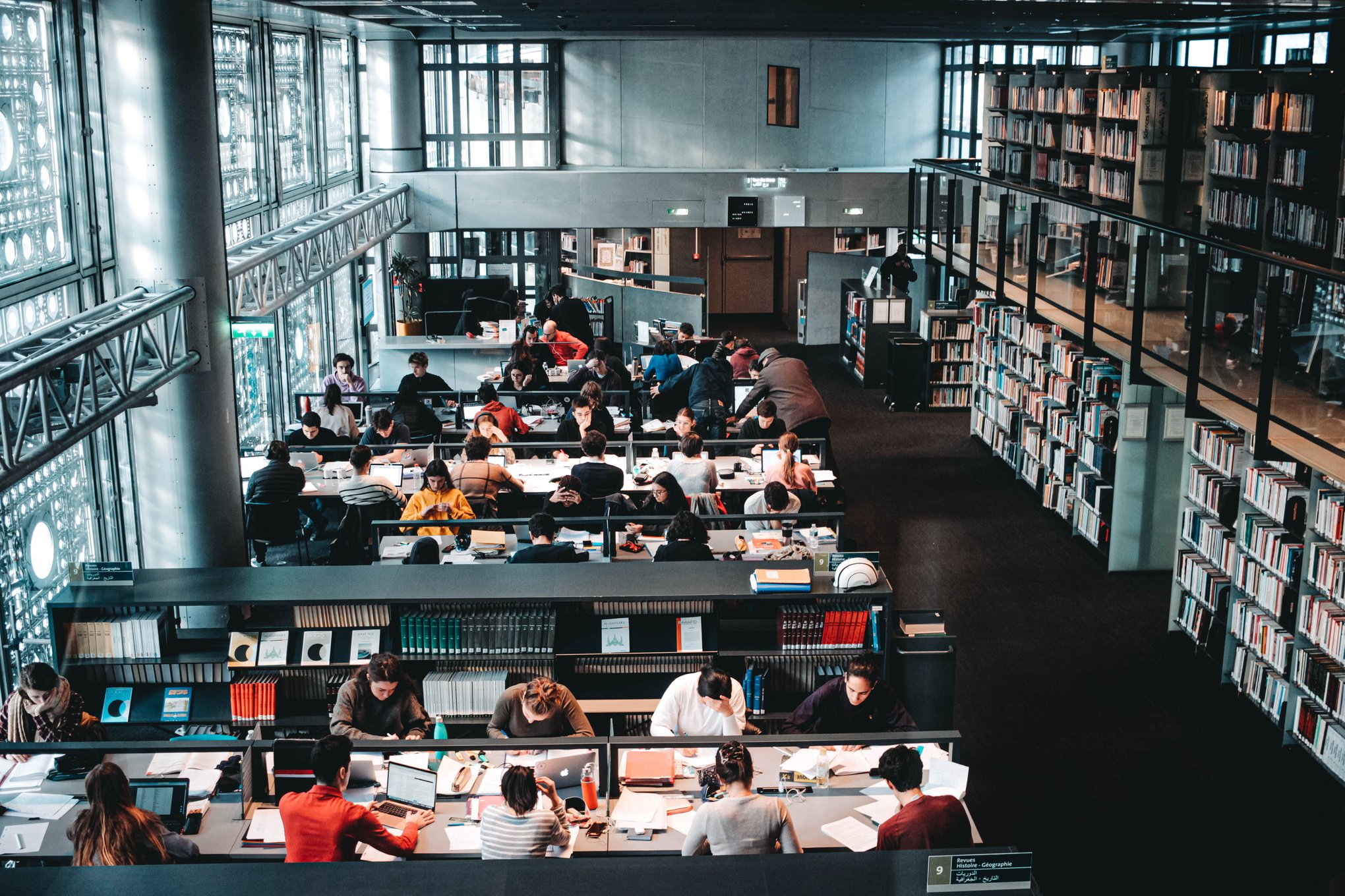 Unrecognizable students with laptops and books studying in public library